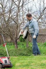 Man pours out of the trimmed grass under a tree to fertilize the soil