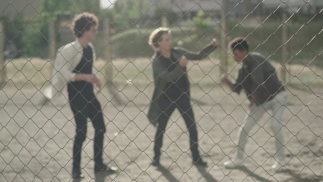 Wide shot of three blurred guys dancing break-dance and robot-dance at sunset. Positive young men enjoying sunny summer day in 1980s or 1990s. Focused at mesh fence at front.