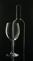 empty glass goblet with black wine bottle on black background with contour lighting