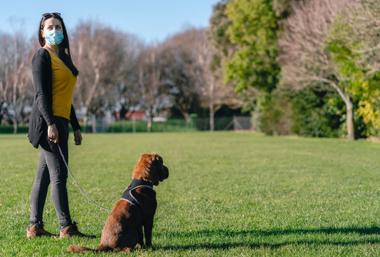 Hispanic Brunette Woman Wearing A Face Mask Going For A Walk With His Dog At The Park