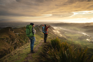 Obraz premium Travel couple standing at the peak of a mountain looking at the horizon. She is opening her arms