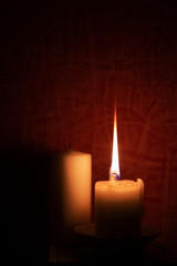 A long flame burning beige candle in the room against a red background. 