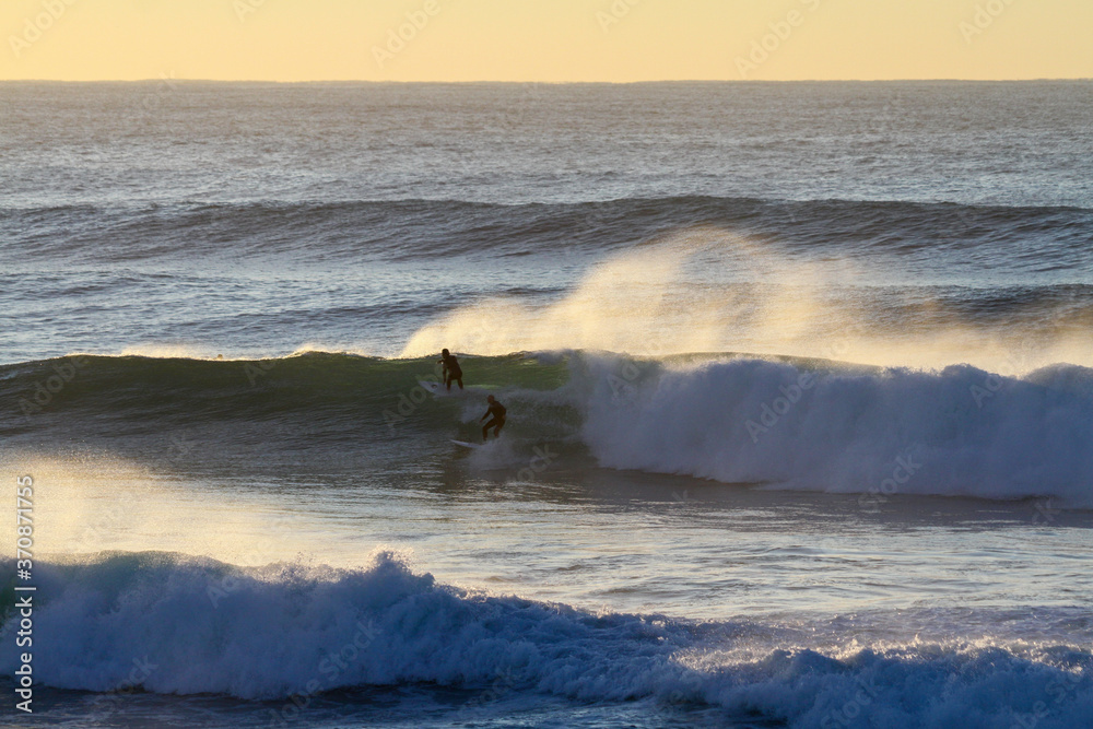 Wall mural Silhouette two surfers on blue ocean wave trying to get barreled at Sunrise