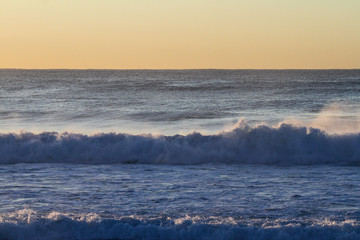 sunrise over the ocean with waves crashing onto the beach, room for text