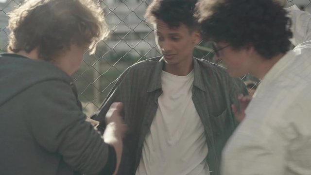 Caucasian hooligans extorting money from African American immigrant in 1980s or 1990s. Confident young criminals taking dollars from threatened bullied guy and leaving. Social problems concept.