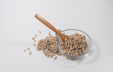 peeled sunflower seeds -shelled- with a wooden spoon and a glass container on white background.