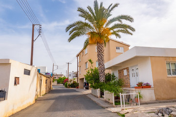 Fototapeta na wymiar Cyprus. The streets of the village of Kouklia. Small houses stand along the road in Cyprus. A palm tree grows next to a one-story house. Kouklia village on a summer day. A trip to Cyprus.