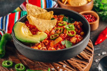 Chili Con Carne in bowl with tortilla chips on dark background. Mexican cuisine.