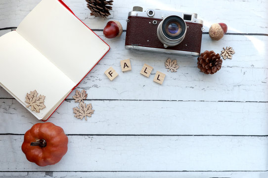 top view of fall-themed elements on a rustic wood surface: vintage camera, open notebook, letters, pumpkin, pinecones, acorns and a scarf with copy space. 
