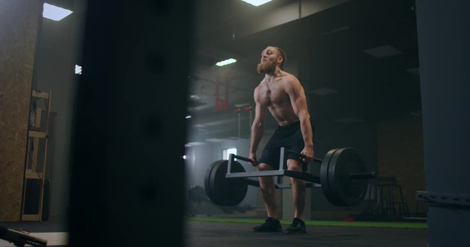 Athletic Beautiful man Does Deadlift with a Barbell in the Gym. Gorgeous male Professional Bodybuilder Workout Weight Lift Exercises in the Authentic Fit Training Facility.