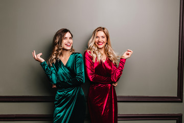 Lovable fair-haired woman in red dress laughing on dark background. Indoor photo of joyful european...