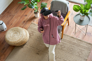 Teen girl pink hair wears vr headset goggles holds controllers plays vr video game futuristic...