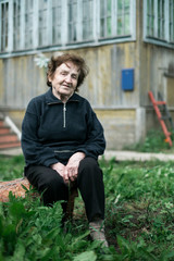 Portrait of an old woman sitting in the courtyard of a rural house.