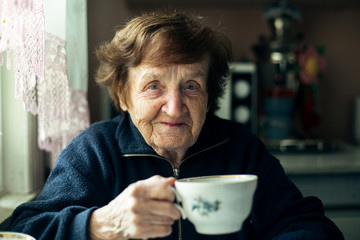 Close-up portrait of an elderly woman drink tea in her home.