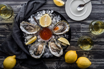 Fresh oysters on a plate of ice garnished with lemon wedges and surrounded by glasses of white wine.