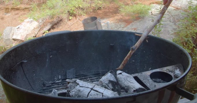 Stick poking and adjusting heated charcoal lumps in a classic kettle grill barbecue