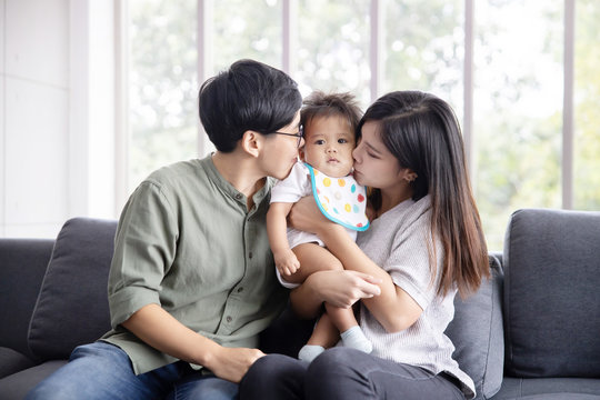 Asian lesbian couple kissing their adopted baby on both cheecks