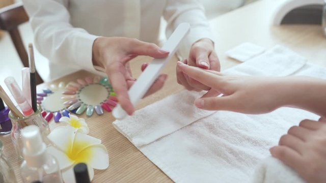 female manicurist doing nail rub by using shiner file tool for woman client in home service. beauty and fashion concept. beautician polishing customer nails with buffer at table indoors.