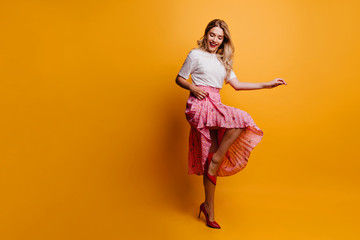 Full-length shot of lovely slim girl in long skirt. Fascinating woman dancing on yellow background.