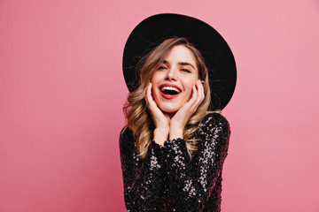 Gorgeous good-looking lady in black hat posing with excitement. Appealing white woman standing on pink background.