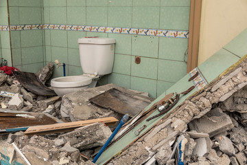A demolished bathroom, with one wall and the toilet still intact. Can represent demolition, war...