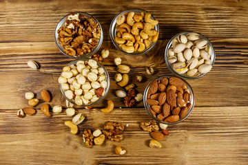 Assortment of nuts on wooden table. Almond, hazelnut, pistachio, walnut and cashew in glass bowls. Top view. Healthy eating concept