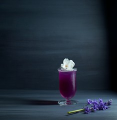 Purple drink garnished with flowers against a dark grey background, butterfly pea flower tea lemonade