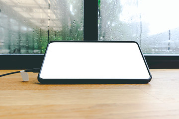 Black smartphone device with blank white screen mockup design template on wood table near glass of window with raindrops in cafe.