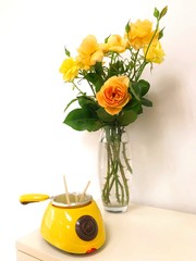 Wax heater. Liquid wax for hair removal flows down on a wooden stick for beauty salon. Vertical photo with yellow flowers - roses. Wax to remove hair from eyebrows, mustaches, face, armpits and legs. 