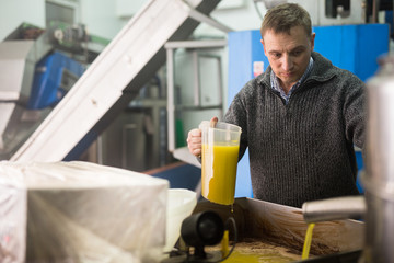 Focused man working in handicraft olive oil producing factory, inspecting first pressing of olives and oil decanting