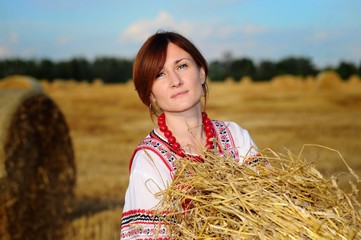Peasant girl in national costume from a white shirt and a red sundress on the field during the harvest