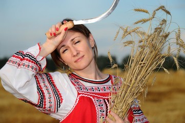 Peasant girl in national costume from a white shirt and a red sundress on the field during the harvest