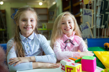 Two funny girls playing with alphabet blocks in the library