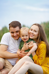 Family life. Portrait of parents and their son on the background of nature. Walk in park. Happy family leisure outdoors.