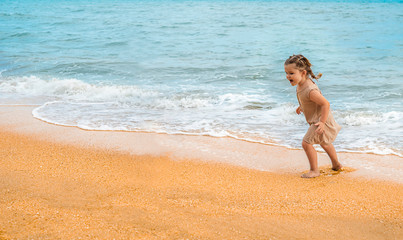 Cute baby on the beach.  Happy girl runs away from the waves.