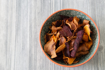 Sweet potato, beetroot and parsnip crisps chips in a patterned bowl.  Grey wood background