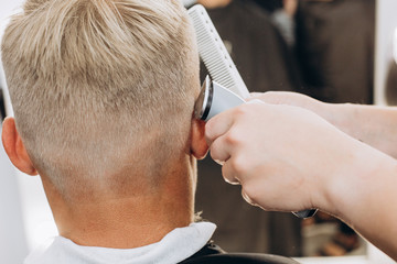 A handsome blond man of European appearance is doing a haircut. Close-up photo. Man at the barber shop