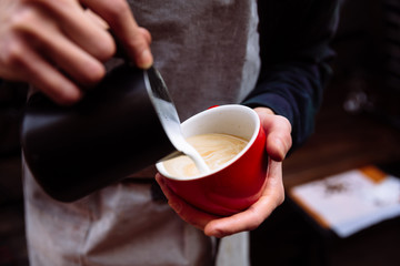 Fototapeta na wymiar Barista pours fresh milk into a cup of coffee. Flower Latte art.