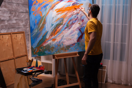 Young man with painting skill working on large canvas in art studio. Modern artwork paint on canvas, creative, contemporary and successful fine art artist drawing masterpiece