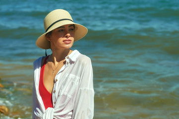 Portrait of a young woman on the sea coast . Beautiful woman in a straw hat by the sea .