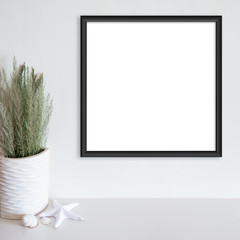 Black frame mockup on white wall with beach/ocean theme decoration on white surface. Copy space.