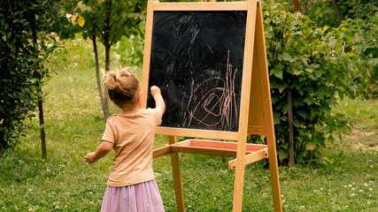 Little girl drawing with chalk at the blackboard side view