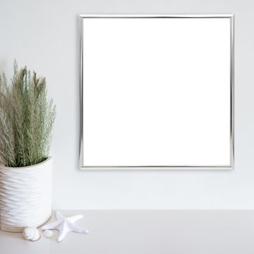 Silver frame mockup on white wall with beach/ocean theme decoration on white surface. Copy space.