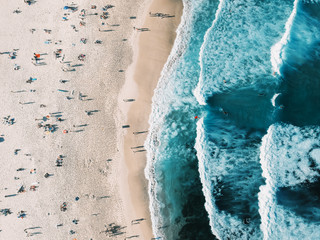 Aerial view of the sea in Australia. Summer seascape with people sunbathing on the beach, under umbrellas, beautiful waves, rocks and sand, turquoise water. Top view from drone