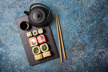 Set of sushi rolls served on a black slate board with chopsticks and asian teapot