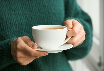Woman with cup of hot tea at home, closeup