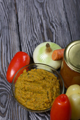 Freshly prepared zucchini caviar in a container. Next to it, canned zucchini caviar in a jar. On the surface of the table vegetables, ingredients for cooking.