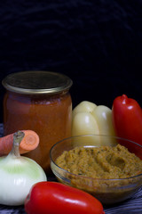 Freshly prepared zucchini caviar in a container. Next to it, canned zucchini caviar in a jar. On the surface of the table vegetables, ingredients for cooking.