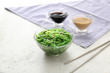 Bowl with tasty seaweed salad and sauces on white background