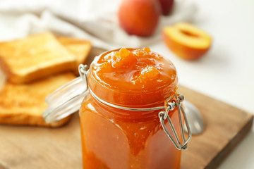 Jar of tasty peach jam on table, closeup